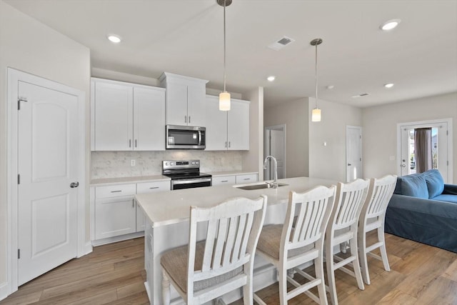 kitchen featuring stainless steel appliances, a sink, tasteful backsplash, light wood-style floors, and open floor plan