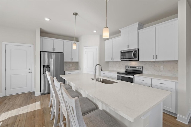 kitchen featuring appliances with stainless steel finishes, a sink, light wood-style floors, an island with sink, and light countertops