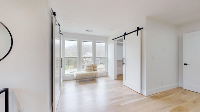 hallway featuring a barn door, light wood-type flooring, and baseboards