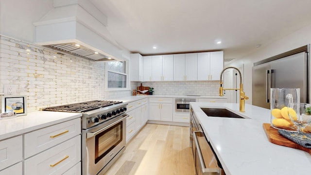 kitchen with high quality appliances, a sink, tasteful backsplash, light wood-style floors, and white cabinetry