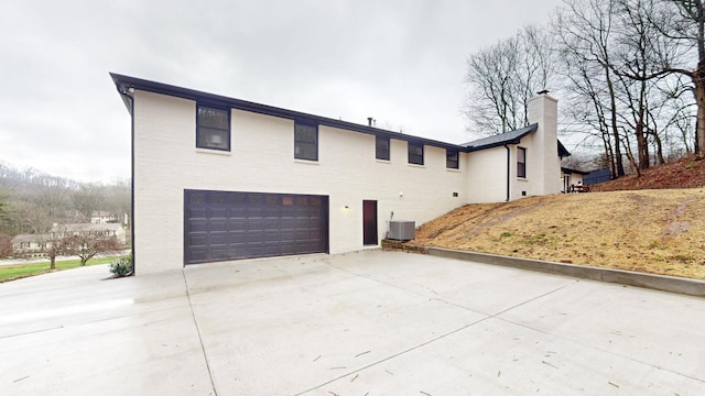 view of front facade with a garage, concrete driveway, a chimney, central AC, and brick siding