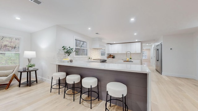 kitchen with a sink, white cabinetry, backsplash, light wood-type flooring, and recessed lighting