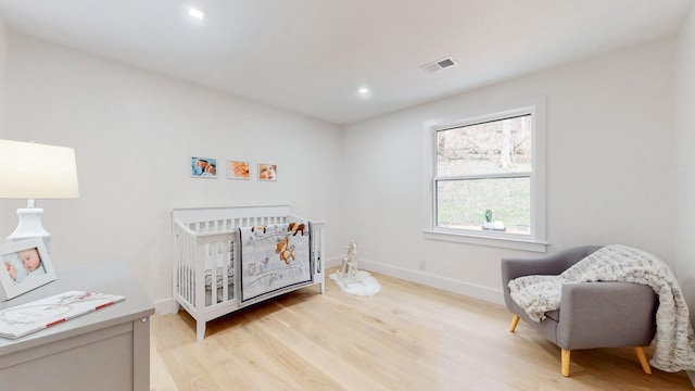 bedroom featuring light wood-style floors, a crib, baseboards, and recessed lighting