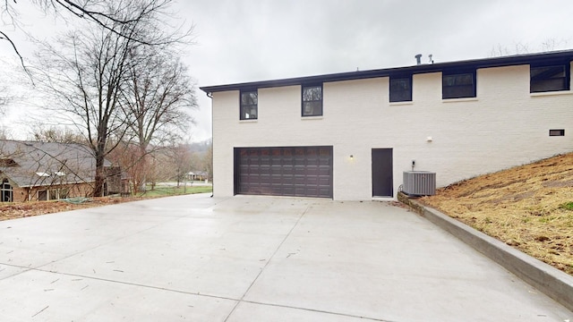 view of side of property featuring an attached garage, driveway, central AC unit, and brick siding