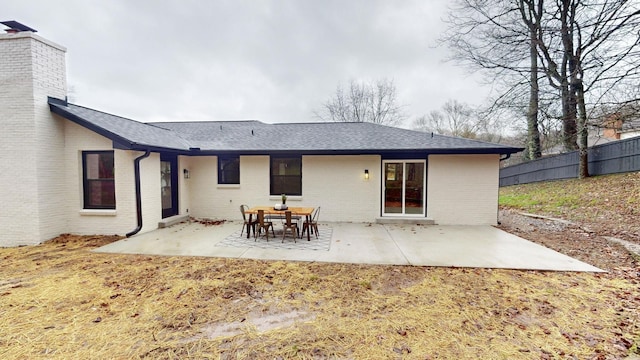 rear view of property with brick siding, a patio area, fence, and a shingled roof