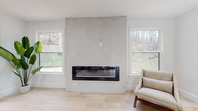sitting room with a glass covered fireplace, wood finished floors, plenty of natural light, and baseboards