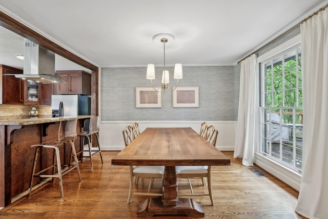 dining room featuring wainscoting, light wood-style flooring, ornamental molding, wallpapered walls, and a chandelier