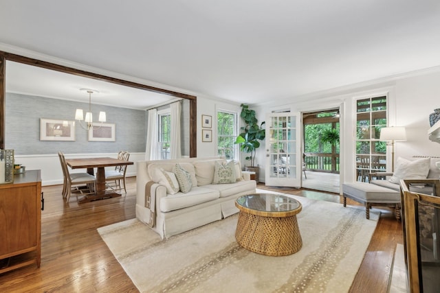 living area with a chandelier, hardwood / wood-style floors, crown molding, and a wainscoted wall
