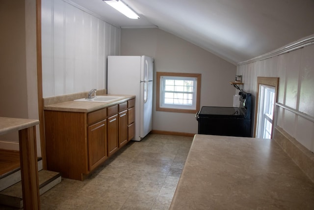 kitchen with black electric range, brown cabinetry, lofted ceiling, a sink, and freestanding refrigerator