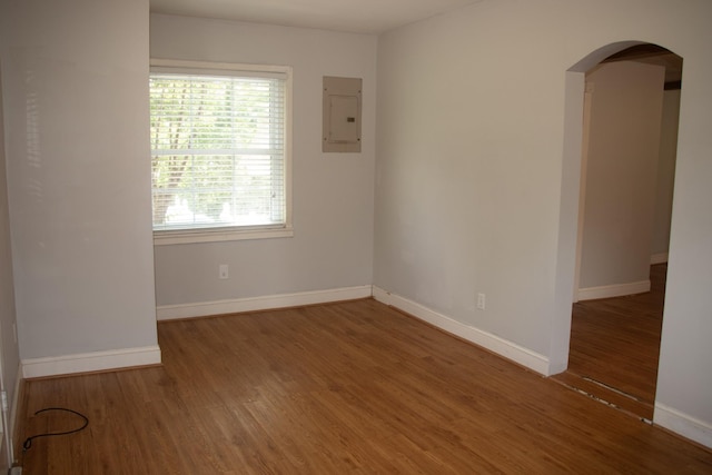 spare room featuring electric panel, arched walkways, wood finished floors, and baseboards