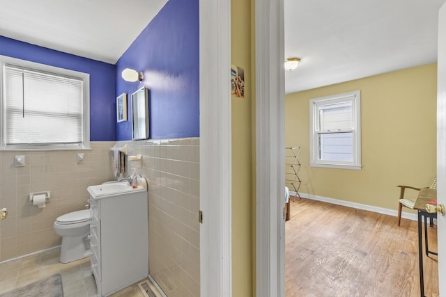 bathroom with toilet, wood finished floors, vanity, tile walls, and wainscoting