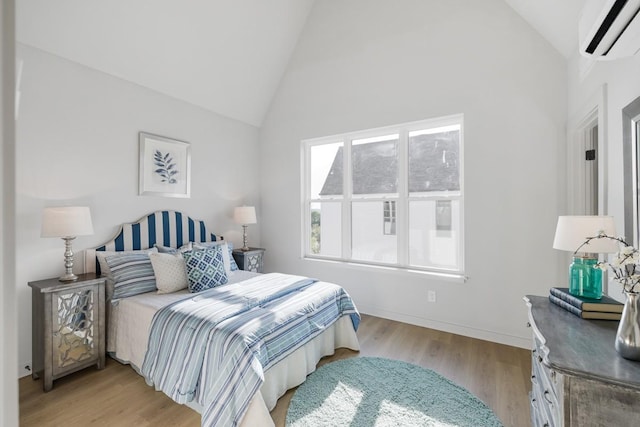 bedroom featuring a wall unit AC, light wood-style floors, high vaulted ceiling, and baseboards