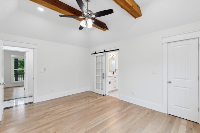 unfurnished bedroom featuring a barn door, light wood-style flooring, baseboards, connected bathroom, and a closet