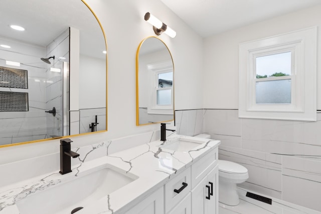 bathroom featuring toilet, plenty of natural light, a marble finish shower, double vanity, and tile walls