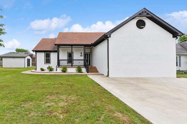 view of front of property with covered porch, a front yard, a storage unit, a shingled roof, and an outdoor structure