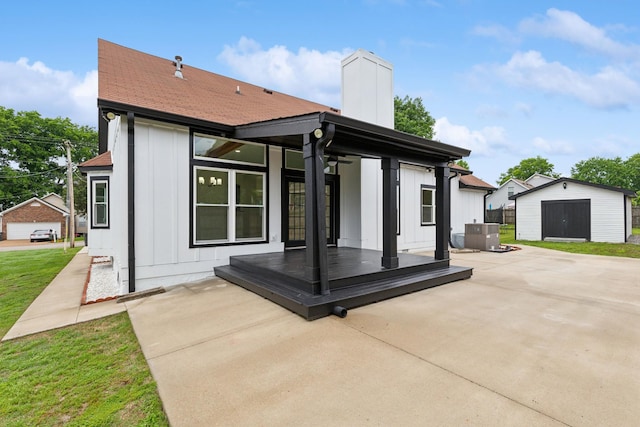 back of house featuring board and batten siding, an outbuilding, a patio, a chimney, and a storage unit