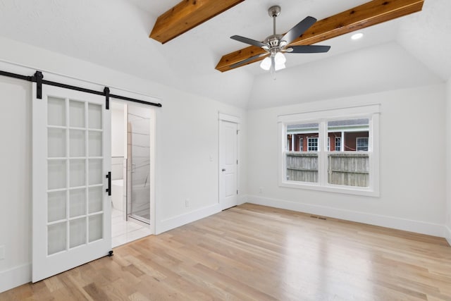 unfurnished bedroom with a barn door, wood finished floors, baseboards, ensuite bath, and a ceiling fan