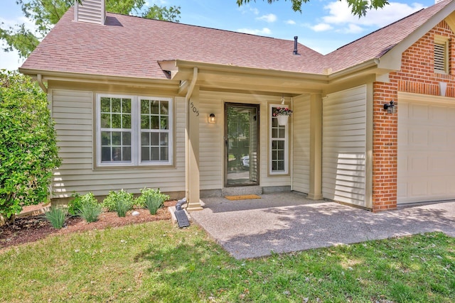 view of exterior entry with a garage, a shingled roof, brick siding, a chimney, and a lawn
