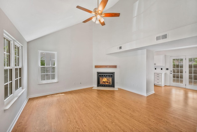 unfurnished living room with light wood-style flooring, a glass covered fireplace, ceiling fan, baseboards, and high vaulted ceiling