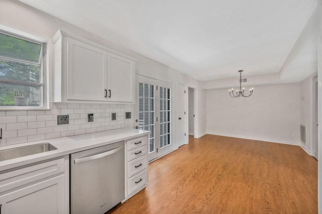kitchen with stainless steel dishwasher, a chandelier, decorative backsplash, white cabinetry, and light countertops