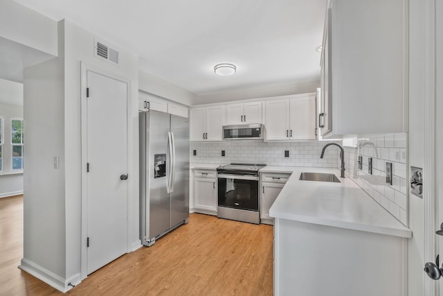 kitchen featuring appliances with stainless steel finishes, a sink, light countertops, and light wood-style floors