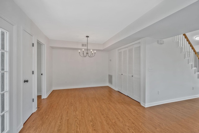 spare room featuring light wood finished floors, a chandelier, baseboards, and stairway