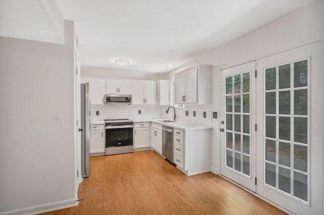 kitchen featuring stainless steel appliances, a sink, light wood-type flooring, tasteful backsplash, and light countertops