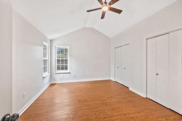 unfurnished bedroom featuring lofted ceiling, two closets, wood finished floors, and baseboards
