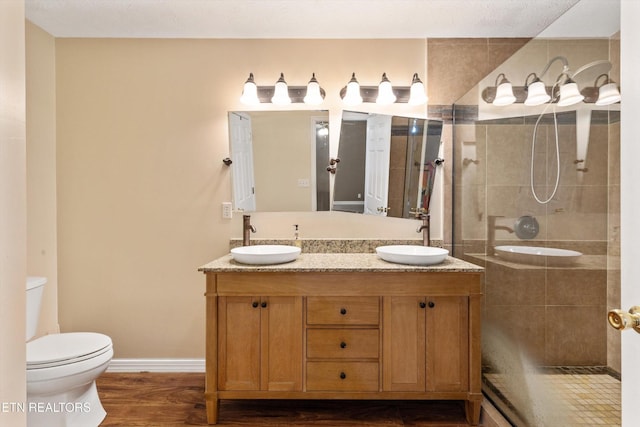338 Lindsey Mill Cir, Rocky Top, TN 37769 - bathroom with toilet, tiled shower, double vanity, wood finished floors, and baseboards