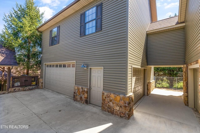 338 Lindsey Mill Cir, Rocky Top, TN 37769 - view of property exterior featuring an attached garage, stone siding, concrete driveway, and fence