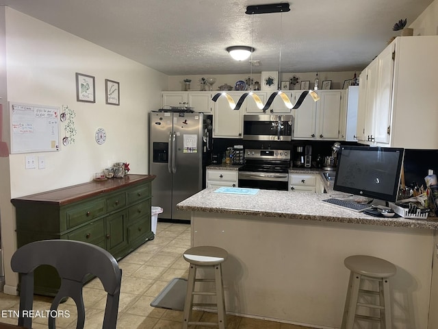 kitchen featuring stainless steel appliances, a peninsula, white cabinets, a kitchen breakfast bar, and a textured ceiling