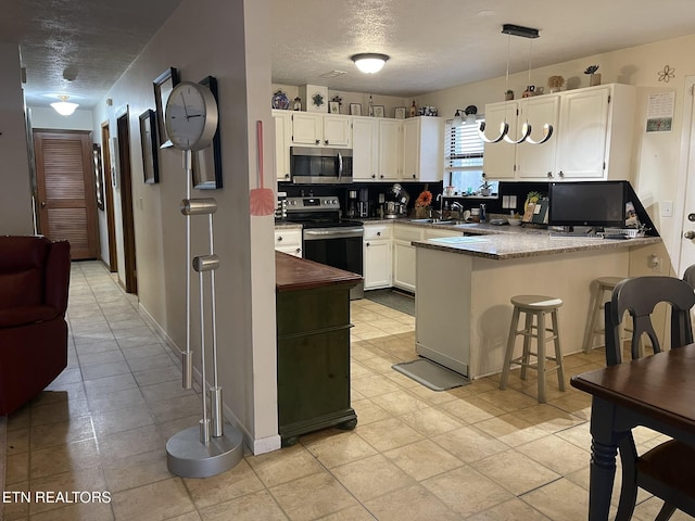 kitchen with appliances with stainless steel finishes, a peninsula, a textured ceiling, a sink, and white cabinets