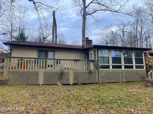 back of property with a chimney, a wooden deck, and a lawn