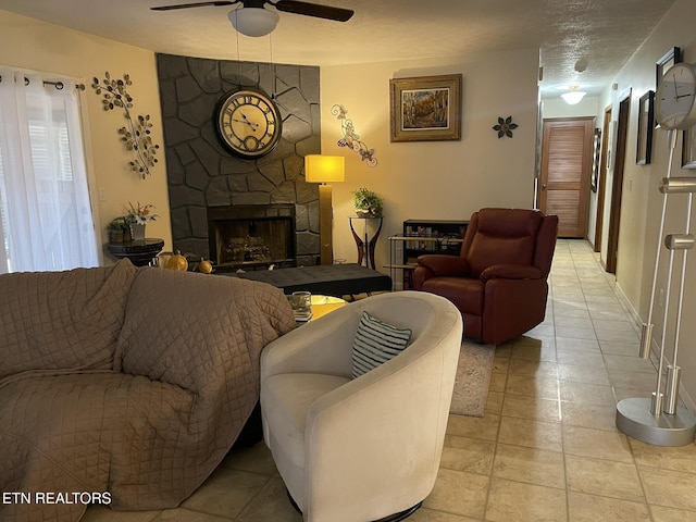 living area with ceiling fan and a stone fireplace