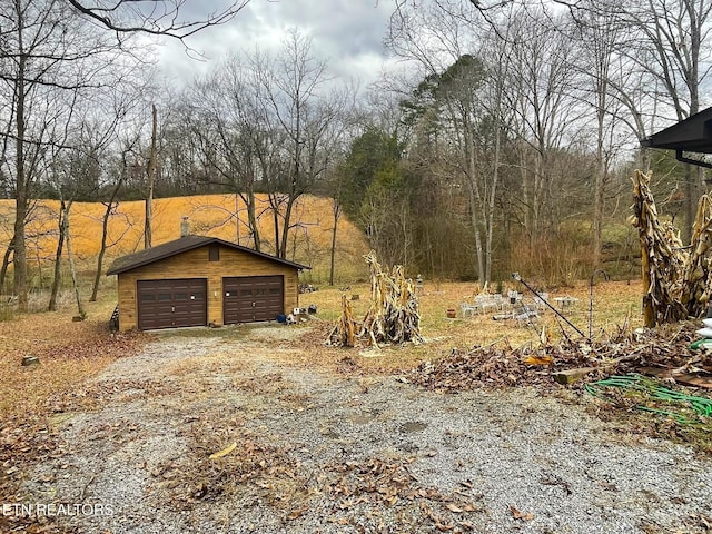 view of yard with an outdoor structure, a detached garage, and driveway