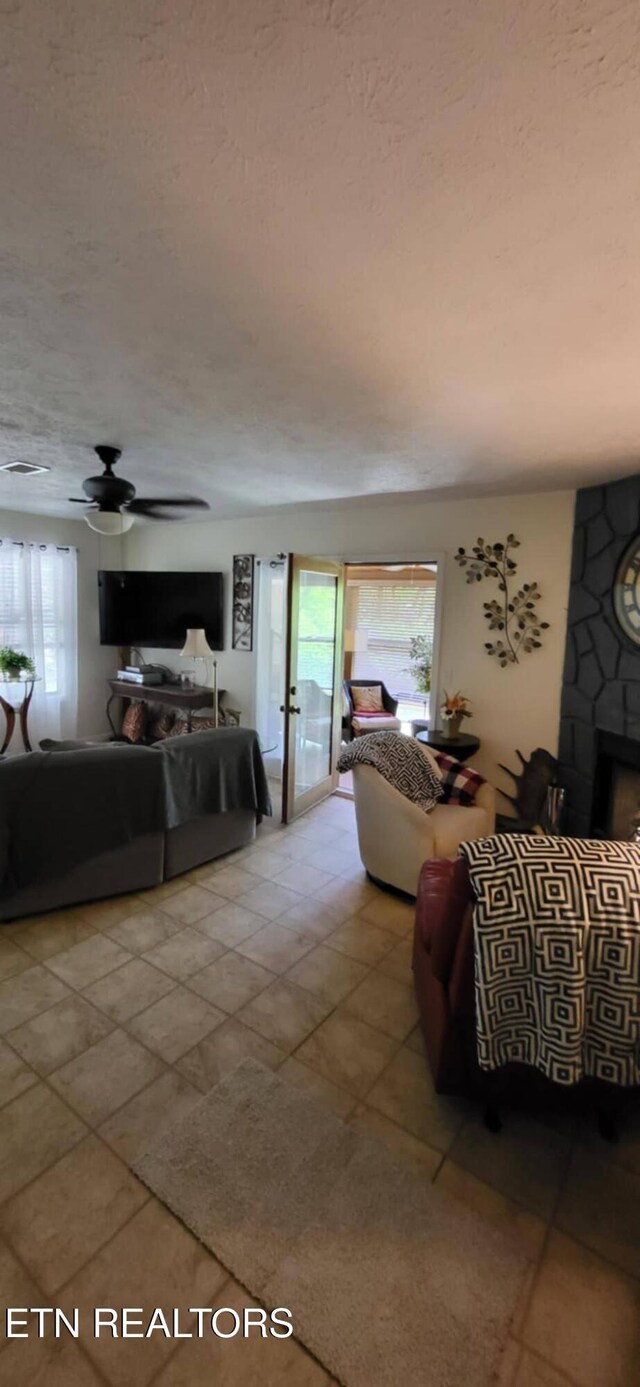 tiled living room with healthy amount of natural light, a fireplace, a textured ceiling, and ceiling fan