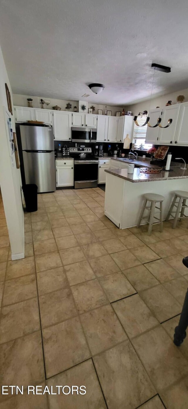 kitchen with appliances with stainless steel finishes, a peninsula, dark countertops, white cabinetry, and light tile patterned floors