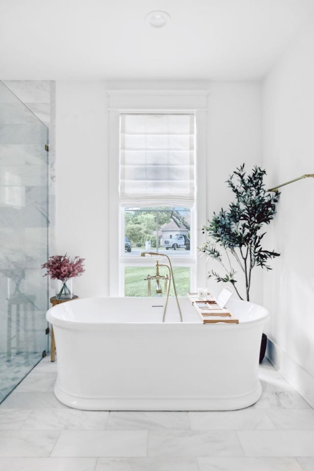 bathroom featuring marble finish flooring, a marble finish shower, and a freestanding tub