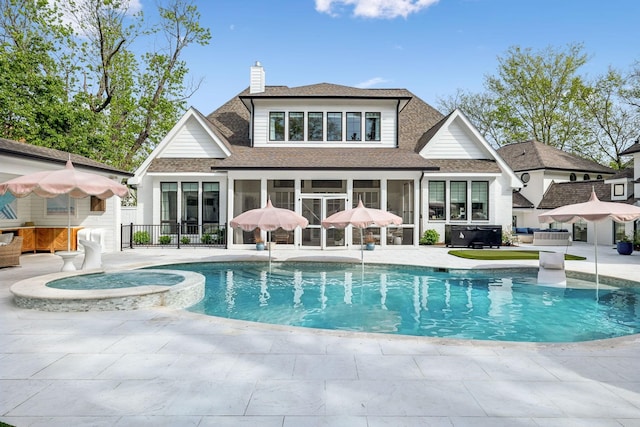 back of property with a patio, a chimney, a shingled roof, a sunroom, and a pool with connected hot tub