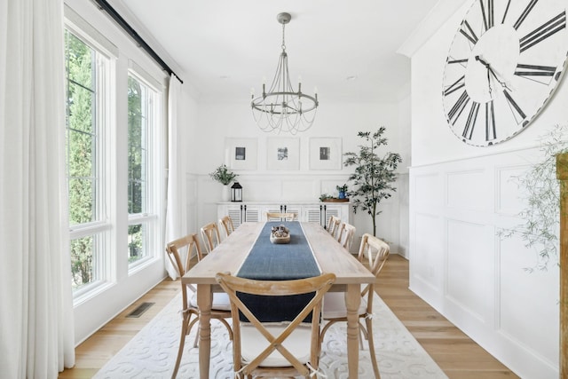 dining space featuring a chandelier, a decorative wall, crown molding, and light wood-style floors