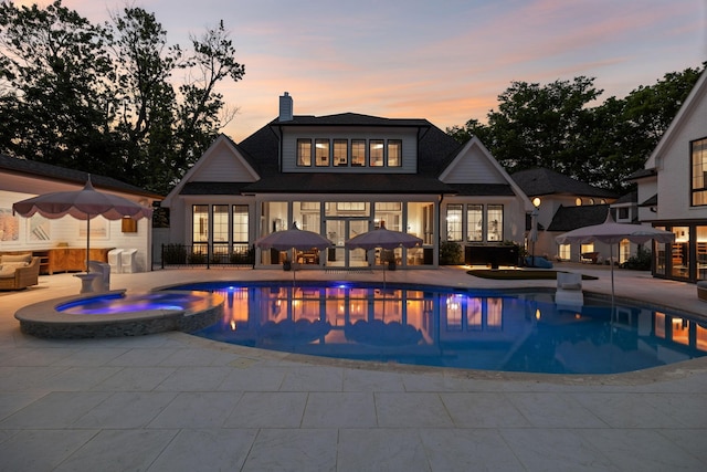 back of house at dusk featuring a patio, a pool with connected hot tub, a chimney, and french doors