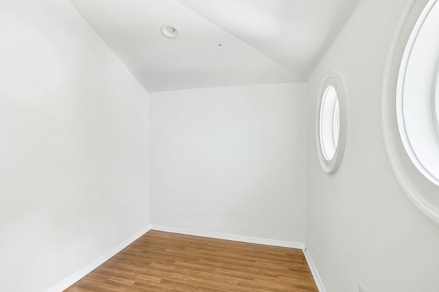 empty room featuring vaulted ceiling, wood finished floors, and baseboards