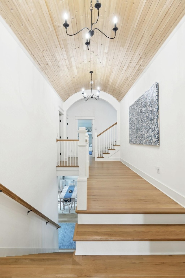 stairs featuring a chandelier, lofted ceiling, baseboards, wood finished floors, and wooden ceiling