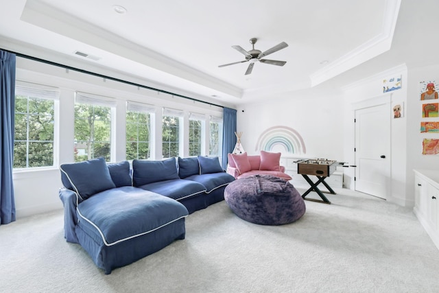 carpeted living room with a raised ceiling, a ceiling fan, and crown molding