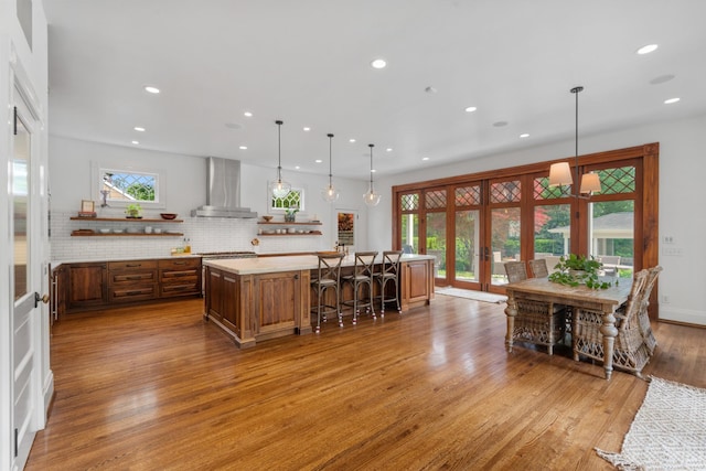 kitchen featuring wall chimney exhaust hood, a spacious island, light countertops, light wood-style floors, and recessed lighting