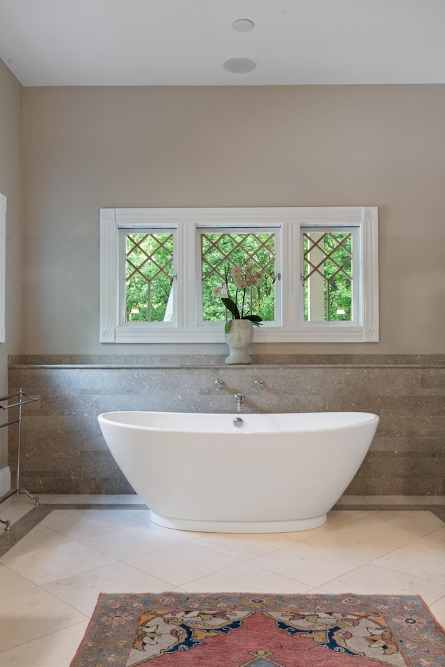 full bathroom with tile walls, healthy amount of natural light, a soaking tub, tile patterned flooring, and wainscoting