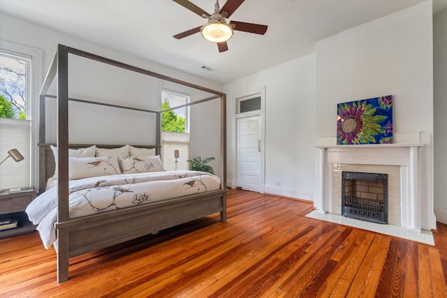bedroom featuring multiple windows, a fireplace with flush hearth, wood finished floors, and baseboards