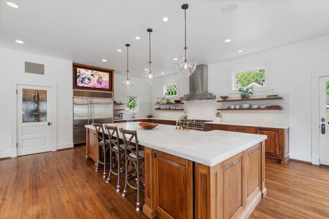 kitchen featuring wall chimney exhaust hood, high end appliances, open shelves, wood finished floors, and recessed lighting