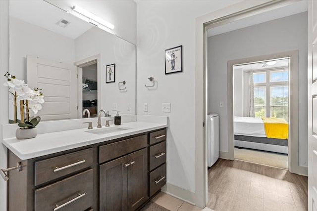 ensuite bathroom with baseboards, vanity, washing machine and dryer, and wood finished floors
