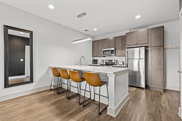 kitchen featuring stainless steel appliances, a peninsula, a breakfast bar, a sink, and dark wood finished floors